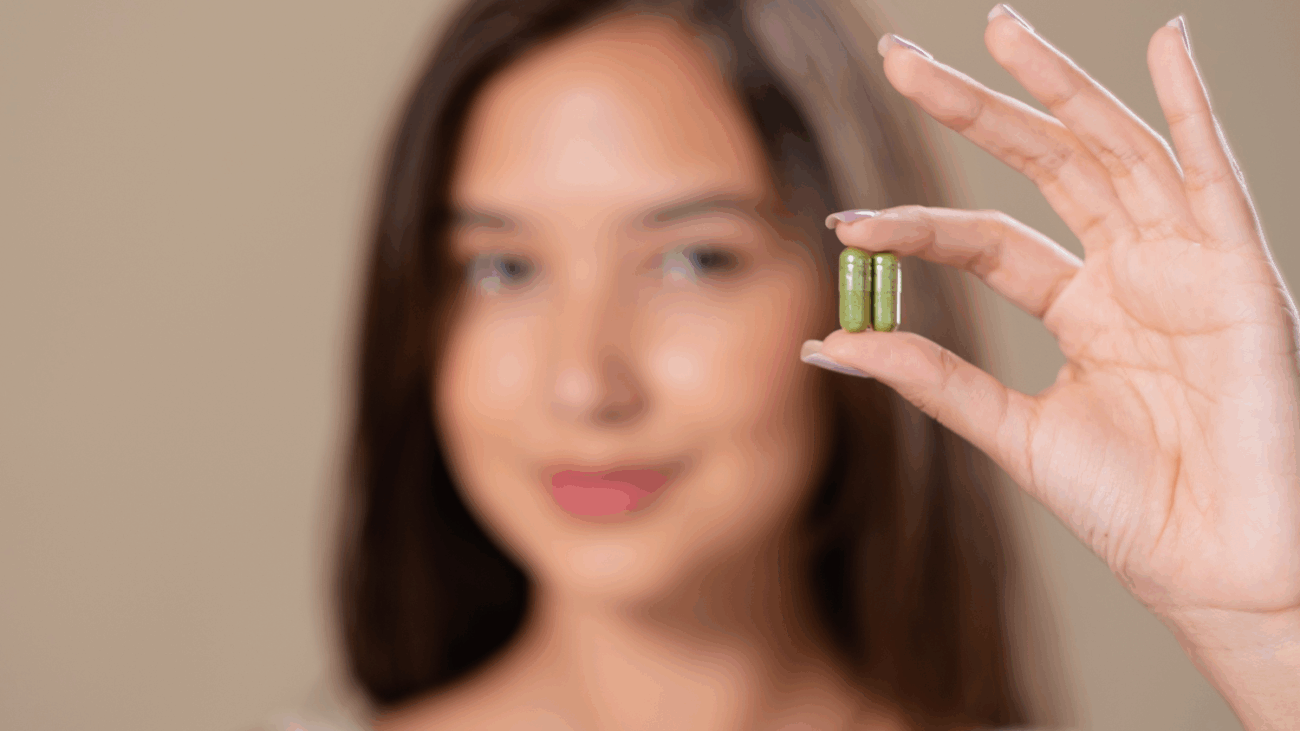 Kobieta trzymająca w dłoni kapsułki suplementów.